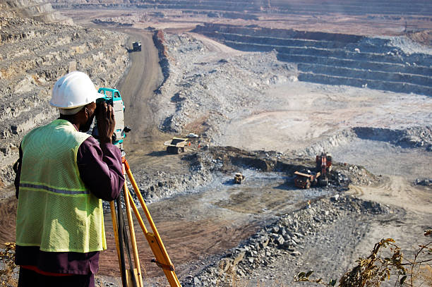 "A locally employed surveyor at an open-pit copper mine in Zambia. He peers through his survey instrument to record the daily changes in the open-pit, and help guide mining activities to the engineer's plans."